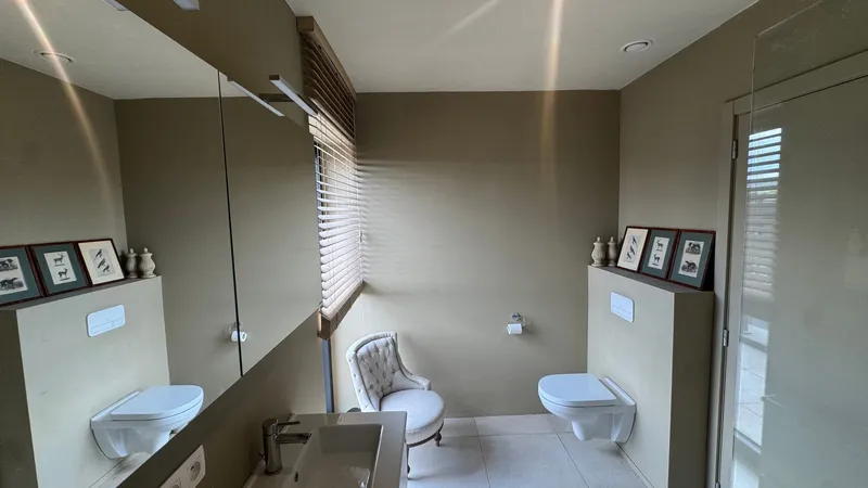 Spacious tiled bathroom with mirrored cabinets and a window in a Ghent apartment