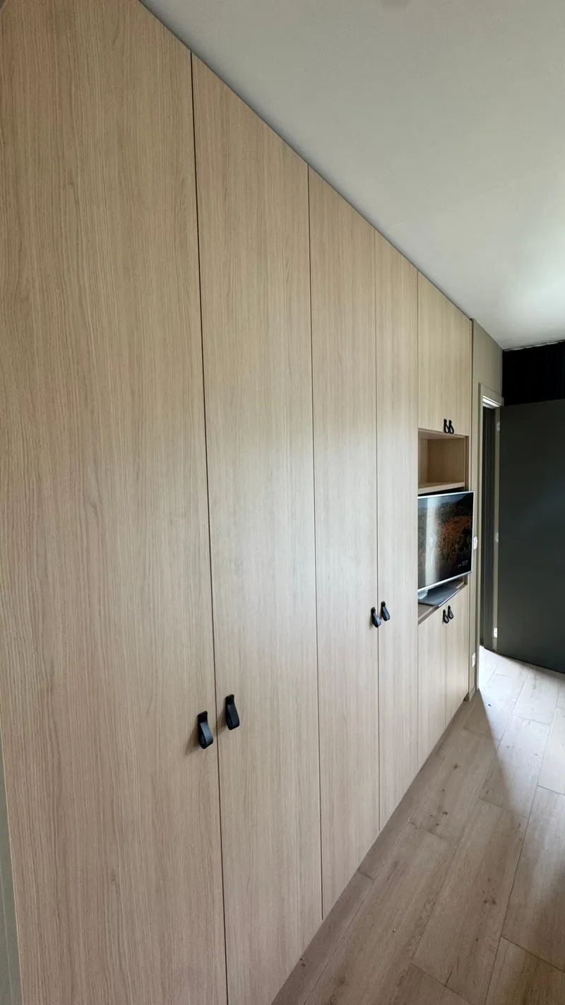 Built-in oak wardrobe wall with leather handles in a Ghent apartment bedroom