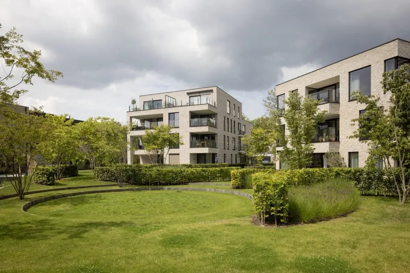 Landscaped communal garden with lawns, young trees and brick apartment buildings at Maple Garden, Ghent