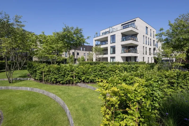 Communal garden with clipped hedges and lawns beside the Maple Garden apartment building under a blue sky, Ghent