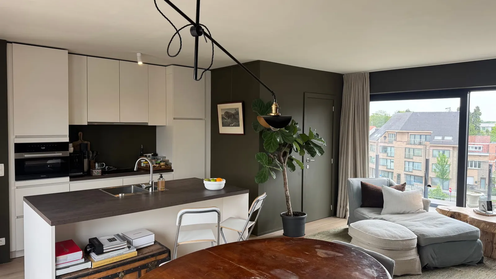 Open-plan living area with kitchen island, lounge seating and city view in a Ghent apartment