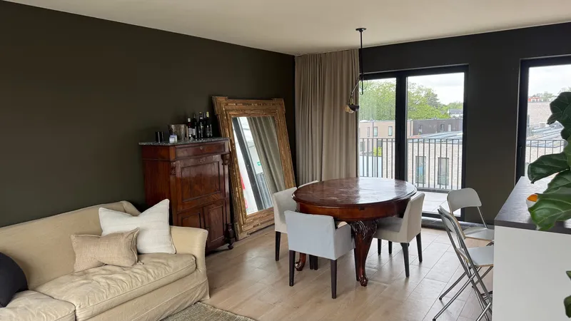 Open-plan living and dining room with balcony doors and a city view in a Ghent apartment